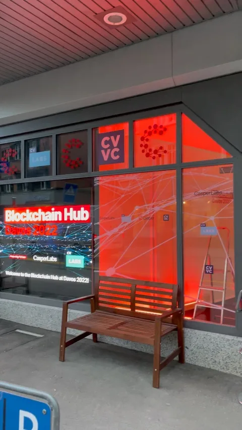 Photo of the actual Blockchain Hub frontage on the Davos Promenade, red window branding glowing at street level