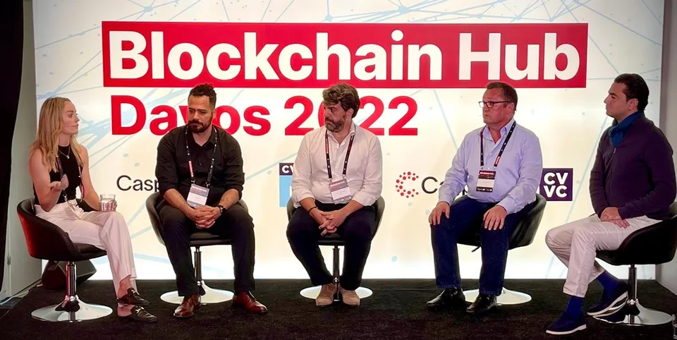 Photo of a five-person panel on the 2022 stage beneath the Blockchain Hub Davos 2022 wall