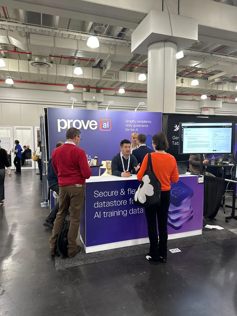 Photo of the finished Prove AI booth on a New York conference floor, attendees mid-demo at the branded counter